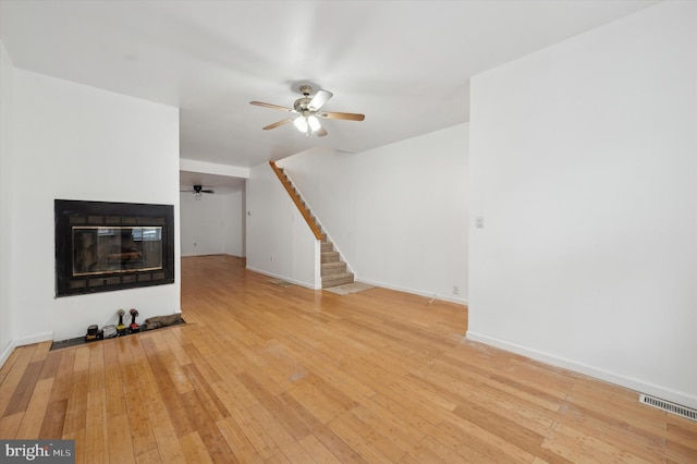 unfurnished living room featuring a multi sided fireplace, ceiling fan, and light hardwood / wood-style floors