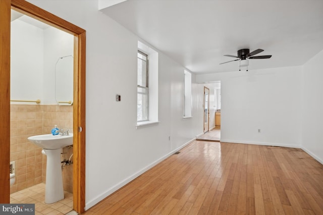 unfurnished living room with tile walls, light wood-type flooring, and ceiling fan