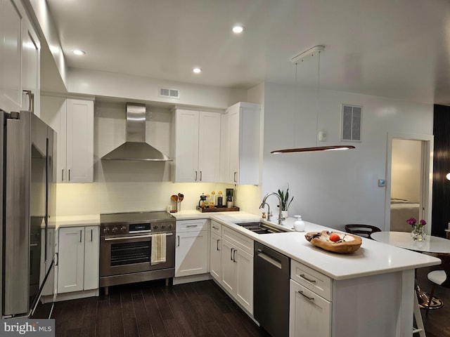 kitchen with a peninsula, wall chimney range hood, visible vents, and stainless steel appliances