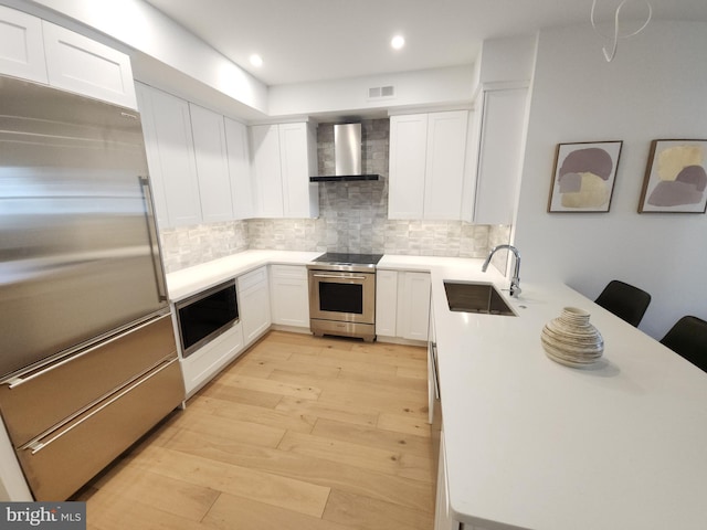 8610 Evergreen Pl Unit 202, Philadelphia, PA 19118 - kitchen with built in appliances, wall chimney exhaust hood, a peninsula, light wood-type flooring, and backsplash