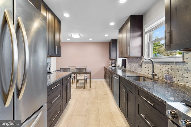 kitchen with dark brown cabinetry, sink, backsplash, dark stone counters, and appliances with stainless steel finishes