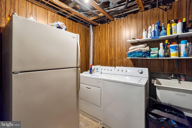 laundry room featuring wood walls, sink, and washer and dryer