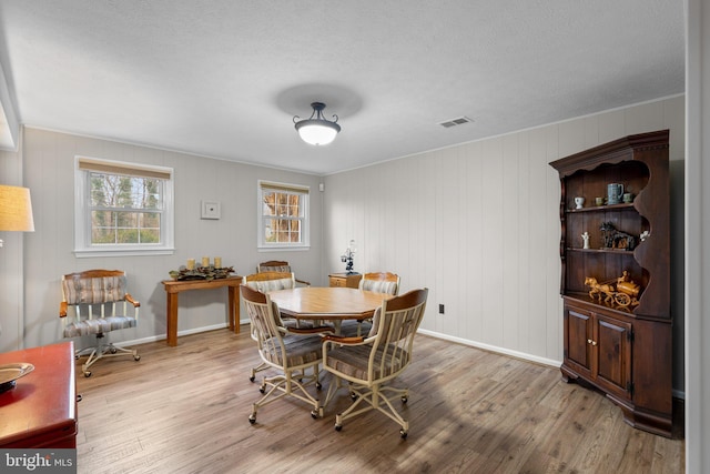 dining room featuring wood walls, light hardwood / wood-style floors, and a textured ceiling