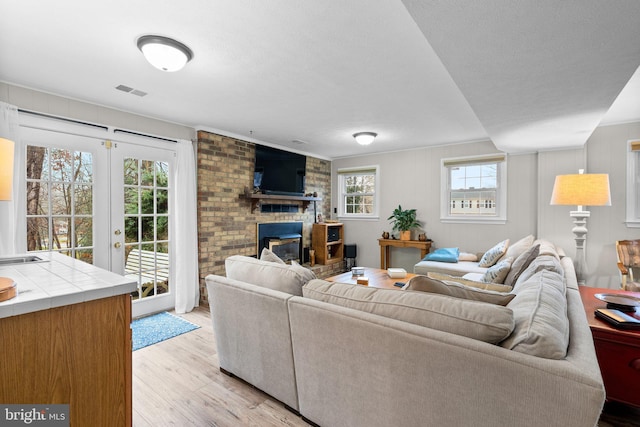 living room with french doors, light hardwood / wood-style floors, a textured ceiling, and a brick fireplace