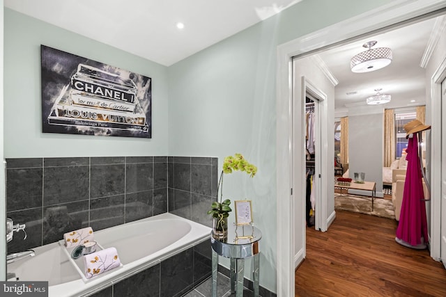 bathroom featuring hardwood / wood-style flooring, a relaxing tiled tub, and ornamental molding