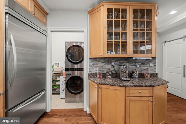 kitchen featuring dark stone countertops, built in fridge, light hardwood / wood-style flooring, and stacked washer / drying machine