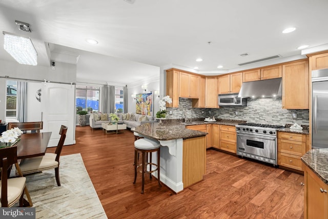 kitchen with a breakfast bar, high end appliances, dark wood-type flooring, and dark stone countertops