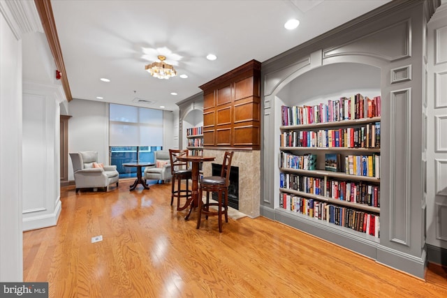 interior space featuring built in shelves, light hardwood / wood-style flooring, ornamental molding, and a premium fireplace