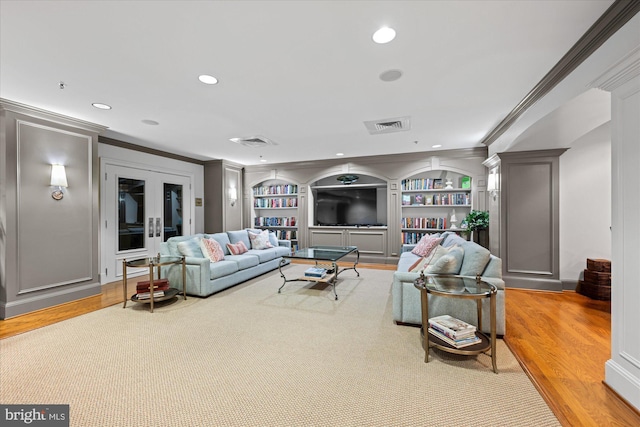 living room with built in shelves, crown molding, french doors, and light hardwood / wood-style floors