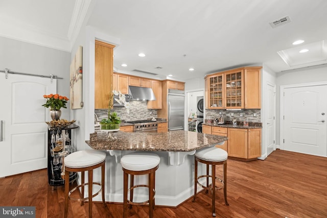 kitchen with tasteful backsplash, dark hardwood / wood-style flooring, dark stone countertops, stacked washer / drying machine, and high end appliances