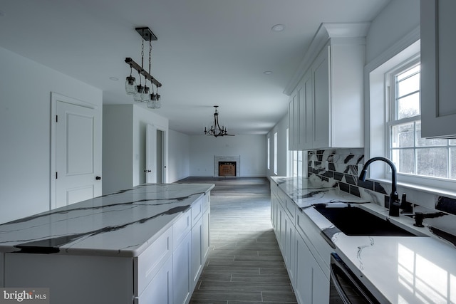 kitchen featuring white cabinets, a fireplace, light stone counters, and sink