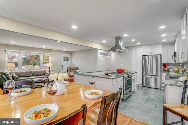 kitchen featuring island exhaust hood, appliances with stainless steel finishes, light stone counters, white cabinets, and an island with sink