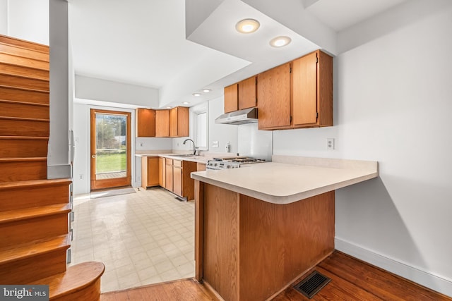 kitchen with kitchen peninsula, stainless steel stove, light hardwood / wood-style floors, and sink