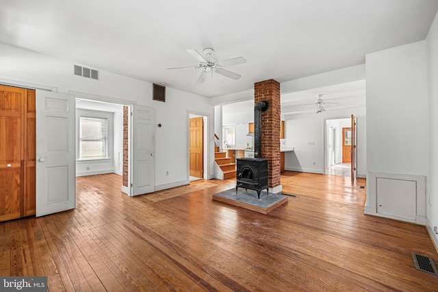 unfurnished living room featuring hardwood / wood-style floors, a wood stove, and ceiling fan