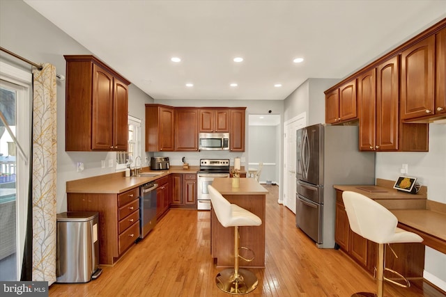 kitchen featuring a kitchen breakfast bar, light wood-type flooring, stainless steel appliances, sink, and a center island