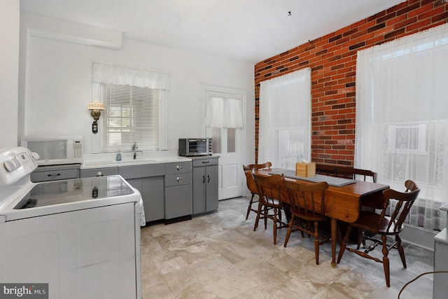 kitchen with gray cabinetry, range, sink, and brick wall