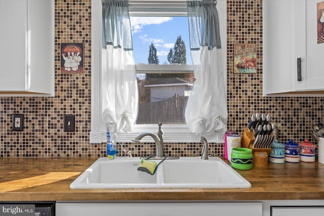 kitchen featuring white cabinets, dishwashing machine, sink, and wooden counters