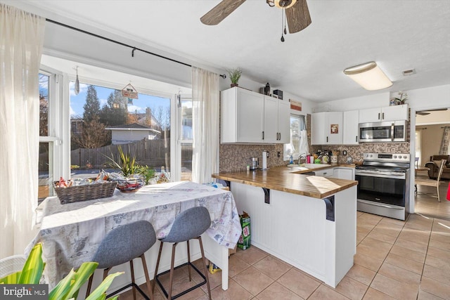 kitchen with a healthy amount of sunlight, white cabinetry, stainless steel appliances, and wood counters