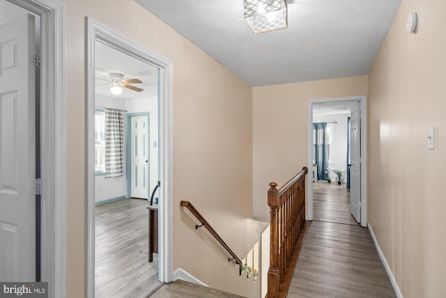 corridor with light wood-type flooring and a textured ceiling