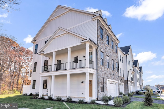 view of front of property featuring an attached garage, a balcony, stone siding, a residential view, and a front lawn