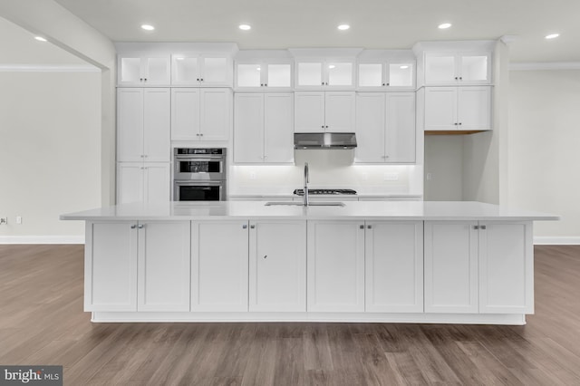 kitchen with light countertops, a large island, glass insert cabinets, and under cabinet range hood