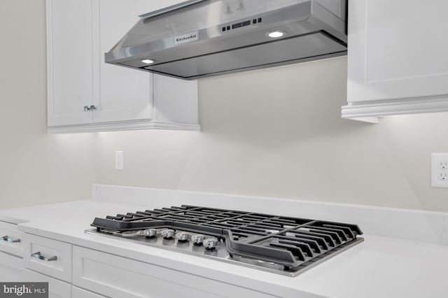 interior details with stainless steel gas cooktop, light countertops, exhaust hood, and white cabinetry