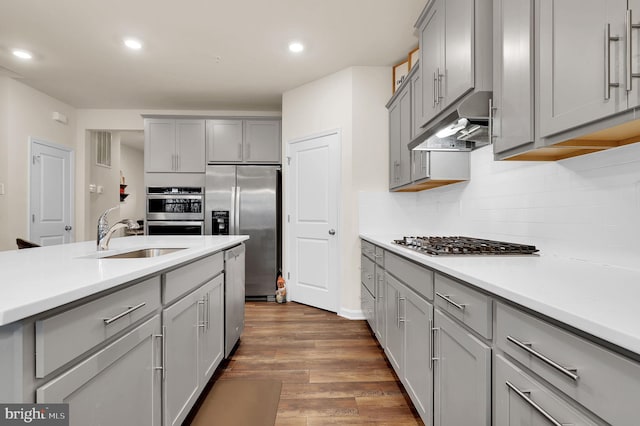 kitchen with decorative backsplash, appliances with stainless steel finishes, dark hardwood / wood-style flooring, sink, and gray cabinets