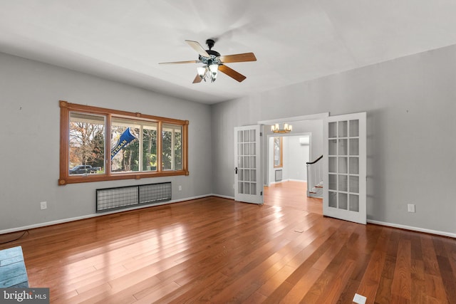 empty room featuring hardwood / wood-style floors, ceiling fan with notable chandelier, radiator heating unit, and french doors