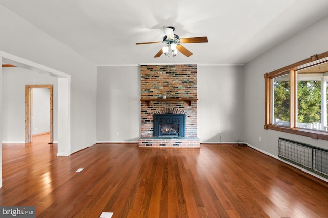 unfurnished living room featuring wood-type flooring, a brick fireplace, ceiling fan, and ornamental molding