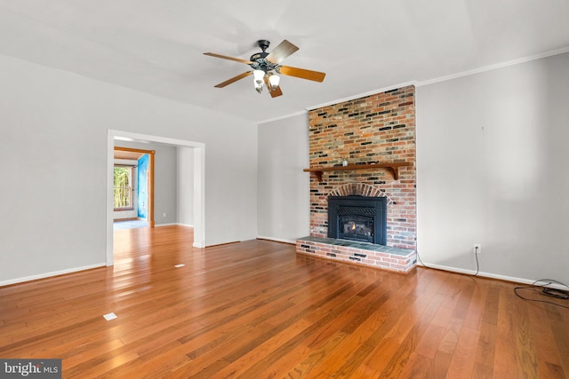 unfurnished living room with ceiling fan, wood-type flooring, crown molding, and a brick fireplace