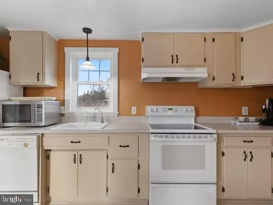 kitchen featuring cream cabinetry, white appliances, decorative light fixtures, and sink