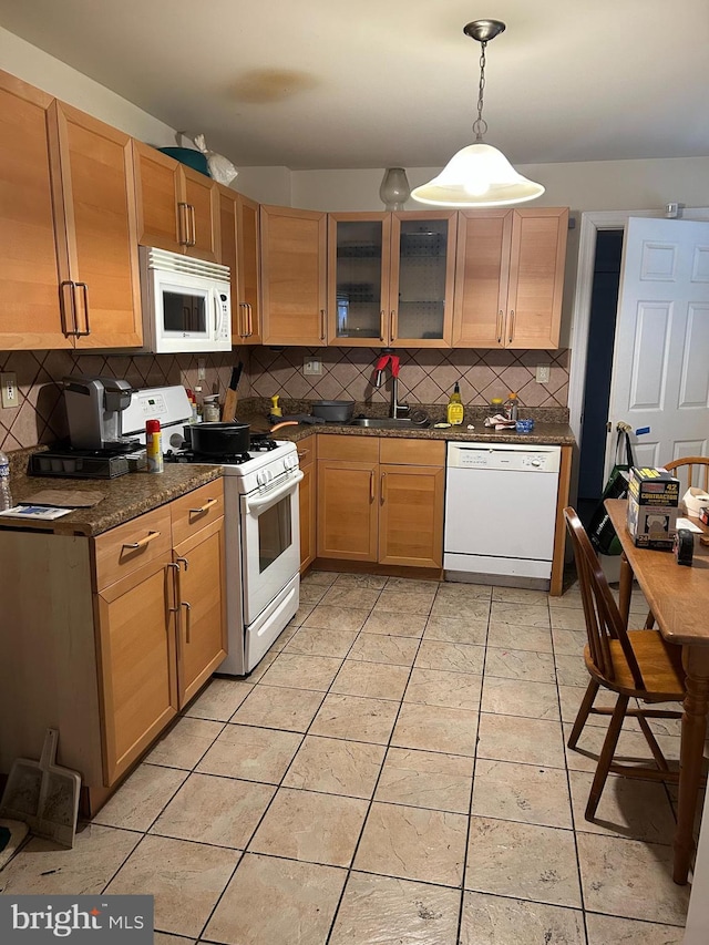 kitchen featuring backsplash, white appliances, light tile patterned floors, dark stone countertops, and hanging light fixtures