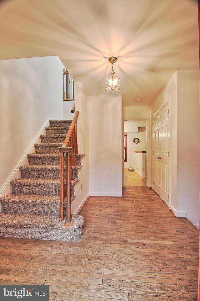 staircase with hardwood / wood-style floors and a chandelier