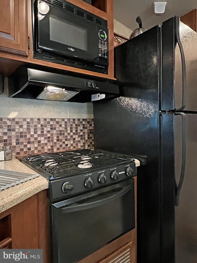 kitchen with backsplash, black microwave, range with gas cooktop, and light stone counters