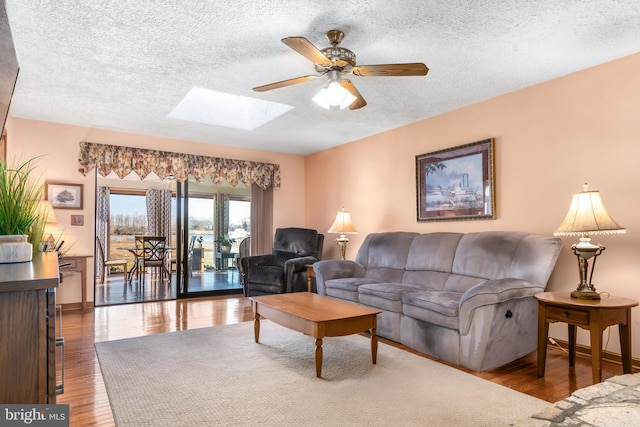 living room featuring ceiling fan, wood-type flooring, a textured ceiling, and a skylight