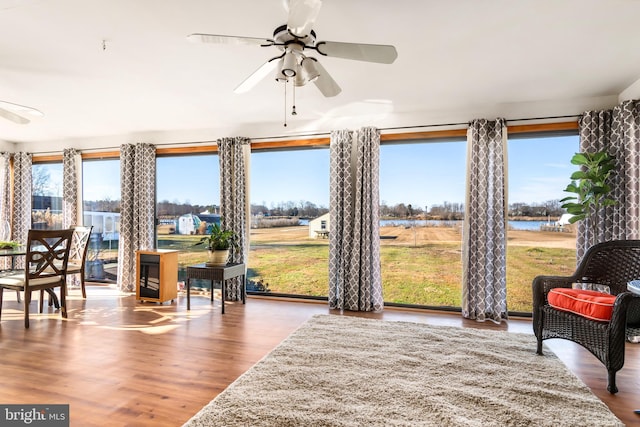 living area with hardwood / wood-style flooring, ceiling fan, and a water view