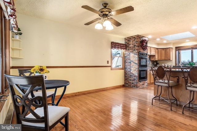 kitchen featuring a skylight, a textured ceiling, double oven, ceiling fan, and light hardwood / wood-style floors