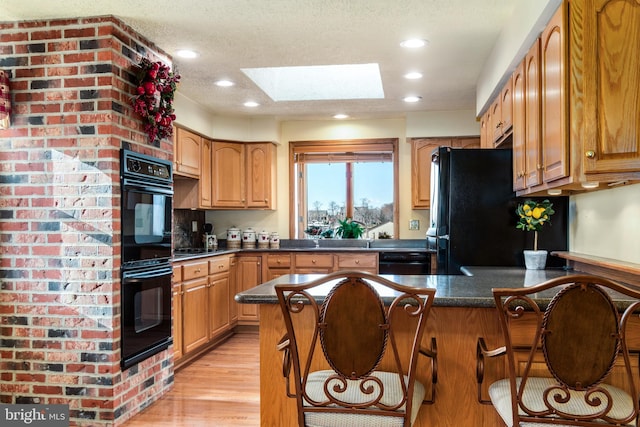 kitchen featuring a skylight, kitchen peninsula, light hardwood / wood-style floors, a breakfast bar area, and black appliances