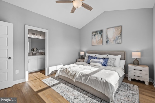 bedroom with ceiling fan, ensuite bathroom, wood finished floors, baseboards, and vaulted ceiling