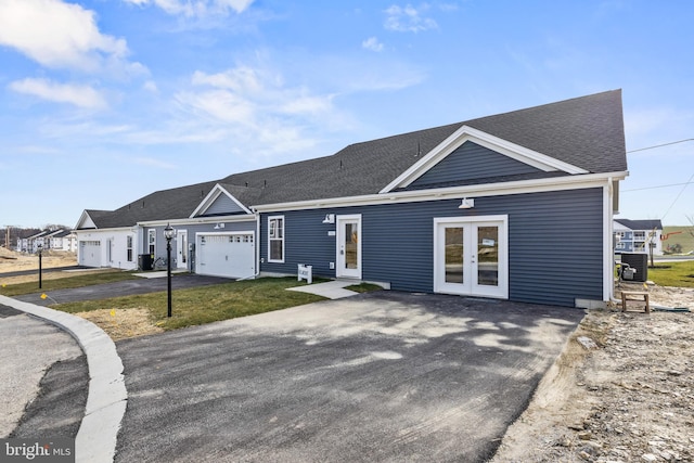 view of front facade featuring aphalt driveway, french doors, roof with shingles, an attached garage, and central AC unit