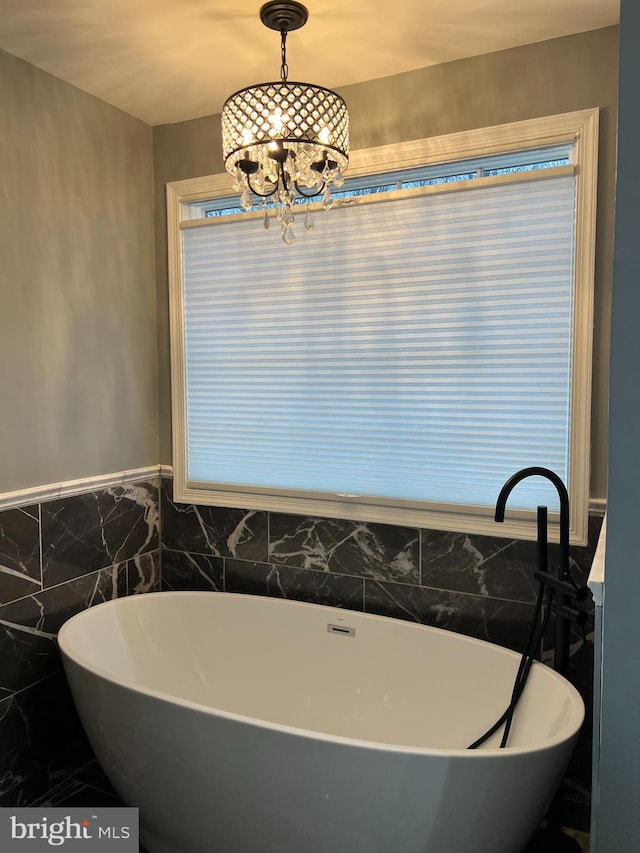 bathroom with an inviting chandelier, tile walls, and a soaking tub