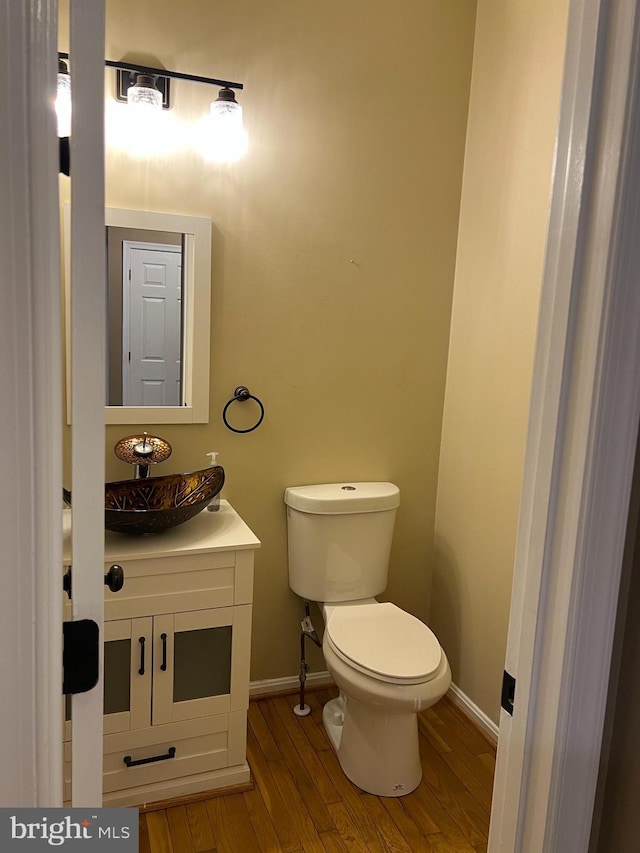 half bath featuring baseboards, vanity, toilet, and wood finished floors