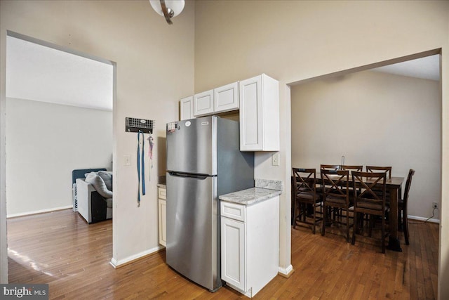 kitchen featuring stainless steel refrigerator, light stone countertops, a high ceiling, dark hardwood / wood-style floors, and white cabinets