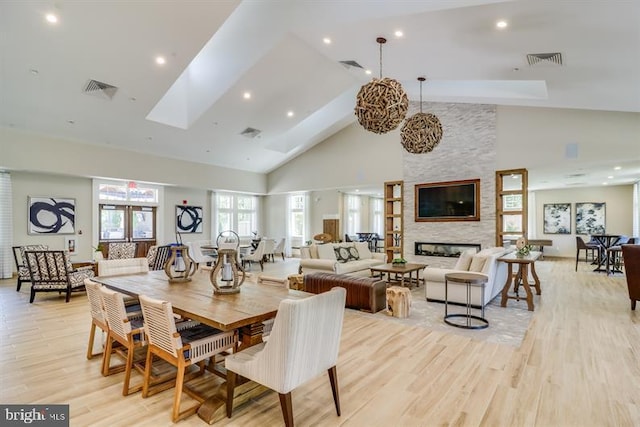 dining room with a stone fireplace, high vaulted ceiling, and light hardwood / wood-style flooring