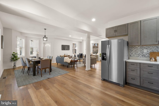 kitchen featuring decorative light fixtures, stainless steel fridge with ice dispenser, backsplash, and light hardwood / wood-style flooring