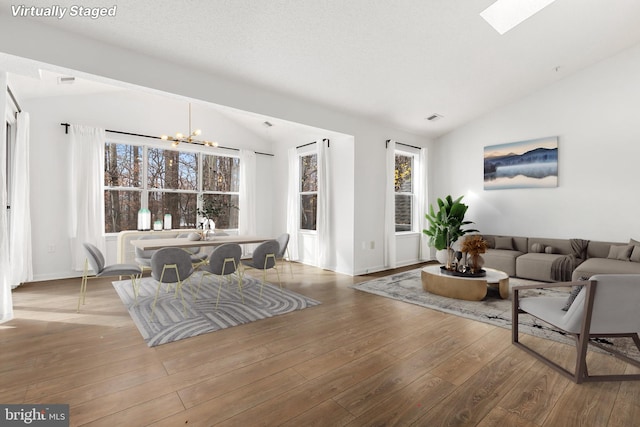 living room featuring lofted ceiling with skylight, an inviting chandelier, and hardwood / wood-style flooring