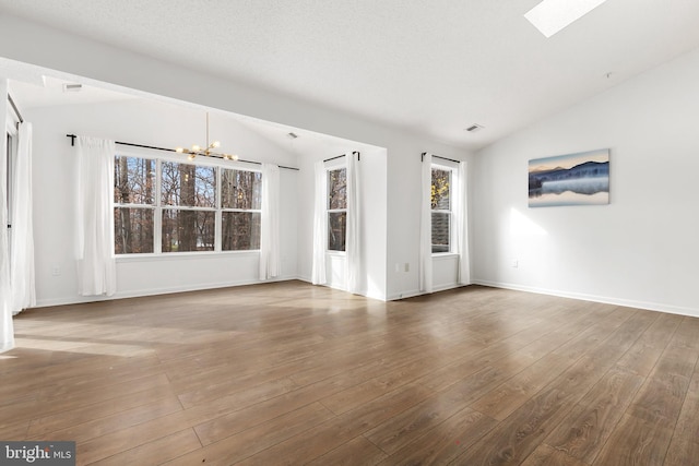 unfurnished room featuring hardwood / wood-style floors, a notable chandelier, and lofted ceiling with skylight