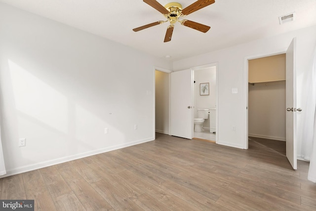 unfurnished bedroom featuring ceiling fan, a spacious closet, light wood-type flooring, connected bathroom, and a closet