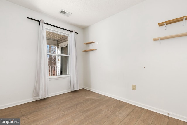 empty room with a textured ceiling and light hardwood / wood-style flooring