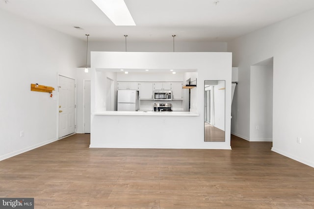 kitchen featuring kitchen peninsula, appliances with stainless steel finishes, decorative light fixtures, white cabinets, and light wood-type flooring